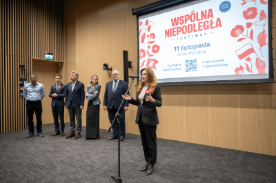 Kobieta w czarnej marynarce przemawia do mikrofonu na tle ekranu z napisem "WSPÓLNA NIEPODLEGŁA".
