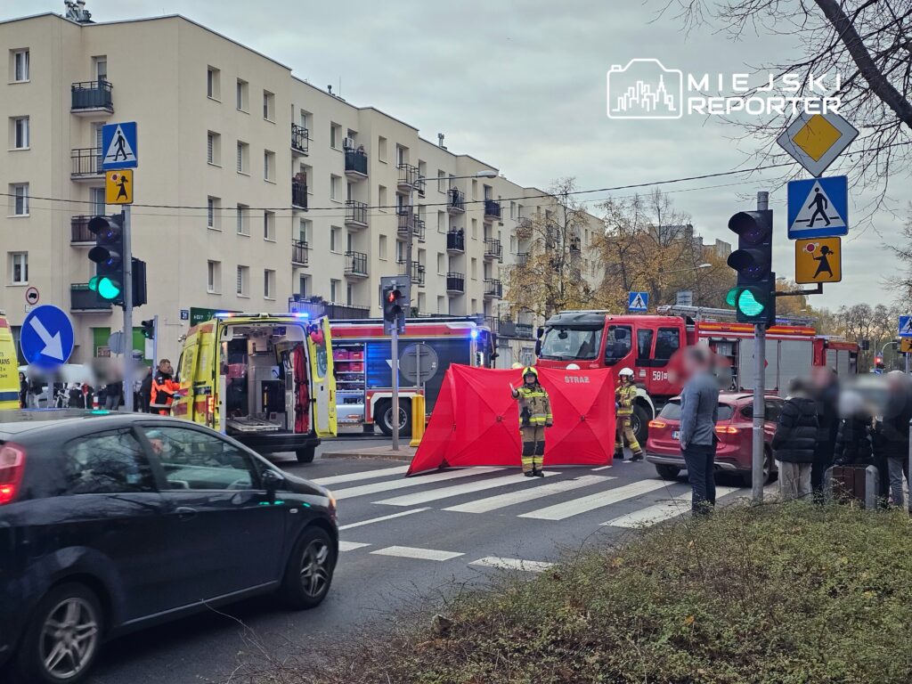 Ratownicy medyczni i strażacy pracują przy wypadku drogowym, z czerwonym namiotem zabezpieczającym na ulicy w mieście.