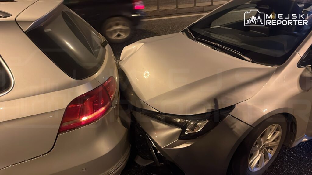 Dwa uszkodzone samochody osobowe zderzone w nocy na ruchliwej ulicy, z widocznymi wgnieceniami na karoserii.