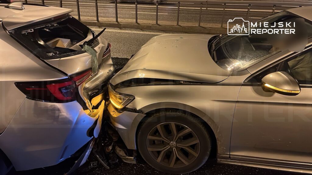 Dwa uszkodzone samochody osobowe zderzone na miejskiej ulicy w nocy, jeden z nich ze złamaną tylną częścią.