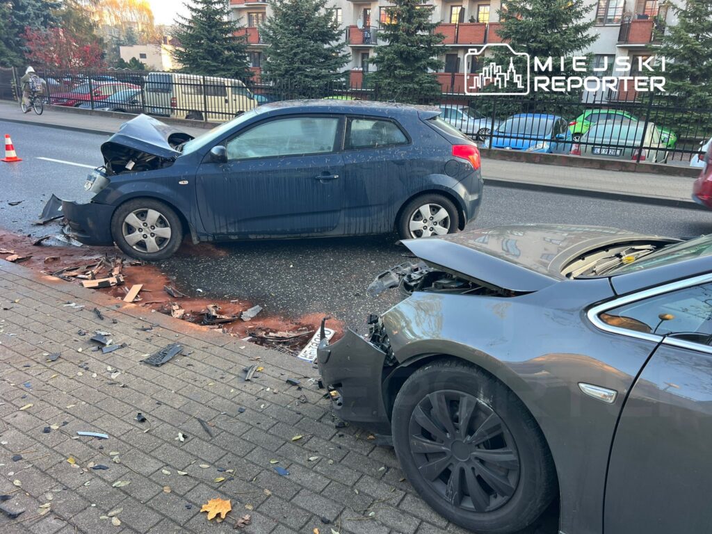 Dwa uszkodzone samochody stoją na ulicy, wokół rozrzucone fragmenty blachy i innych elementów.