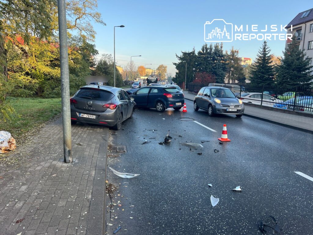 Dwa uszkodzone samochody na jezdni, obok leżą fragmenty karoserii, a na drodze ustawione są trójkąty ostrzegawcze.