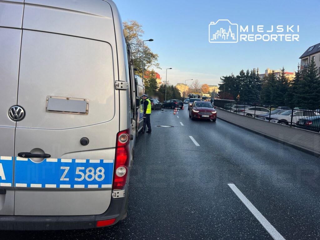 Na drodze stoi policyjny van, a funkcjonariusz rozmawia z kierowcą samochodu osobowego w pobliżu wypadku.