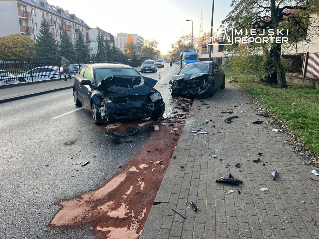 Dwa uszkodzone samochody osobowe na ulicy, wokół leżą fragmenty karoserii i plamy oleju.