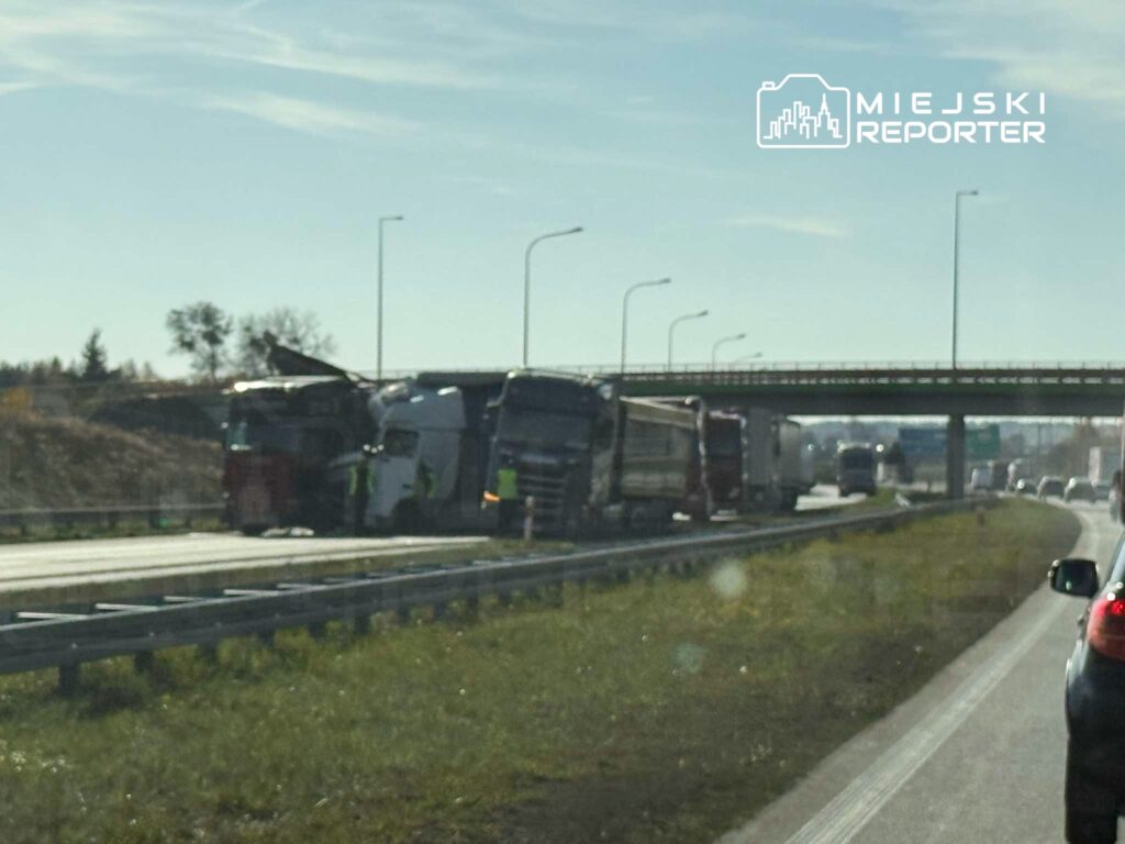 Dwa ciężarówki zderzone na autostradzie, w tle widoczne inne pojazdy i most. Ruch utrudniony.