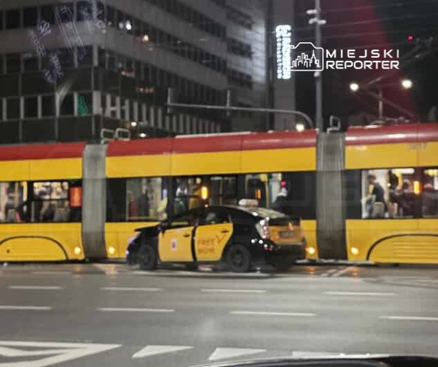 Zielona taksówka zatrzymana obok żółtego tramwaju na ulicy w nocnym otoczeniu miejskim.