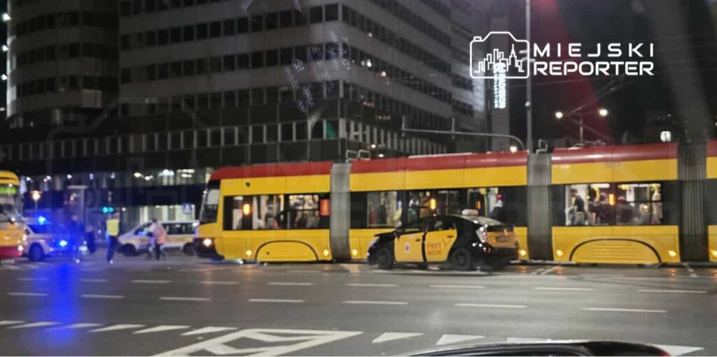 Tramwaj z czerwono-żółtym nadwoziem stoi na skrzyżowaniu, obok policyjne radiowozy i taksówka zaparkowana na jezdni.