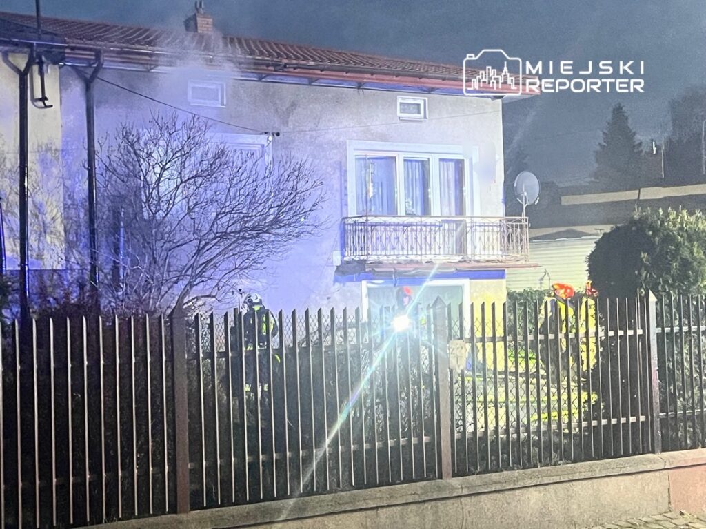 Strażak w hełmie kontrolujący sytuację przy zadymionym budynku mieszkalnym nocą.