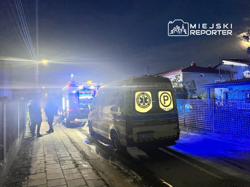 Zespół ratunkowy pracujący przy ambulansie na oświetlonej ulicy w nocy, z widocznymi niebieskimi światłami.