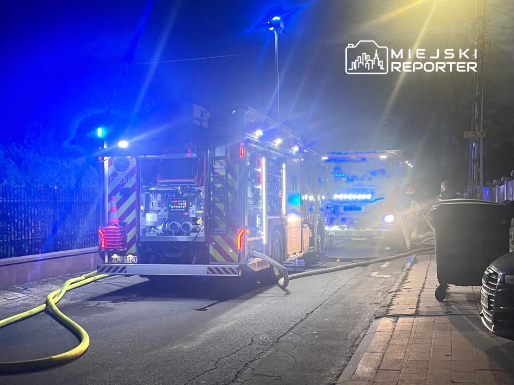 W nocy strażacy przy użyciu wozu strażackiego podłączają wąż do hydrantu na oświetlonej ulicy.