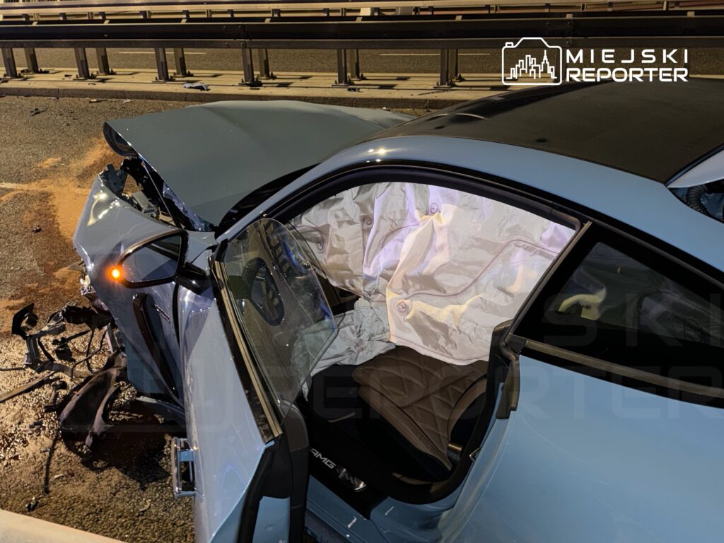 Rozbity samochód osobowy na drodze, z otwartymi drzwiami i poduszką powietrzną w środku.