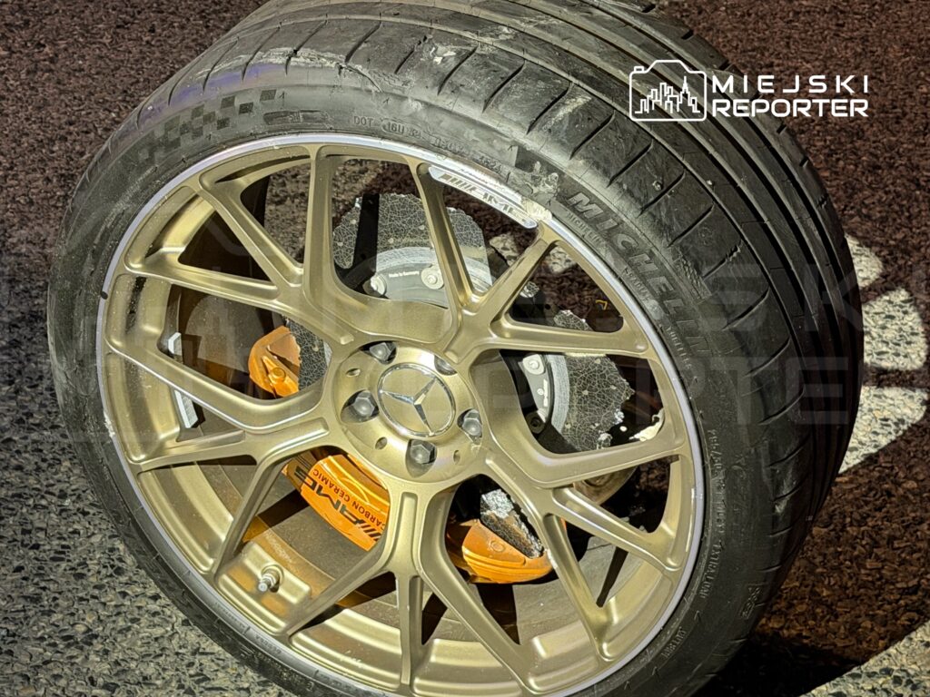 Złota felga samochodowa z oponą Michelin, z widocznymi zaciskami hamulcowymi w kolorze pomarańczowym, leży na asfaltowej nawierzchni.