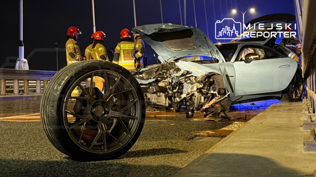 W pobliżu zniszczonego samochodu z otwartą maską, strażacy analizują sytuację na oświetlonym moście.