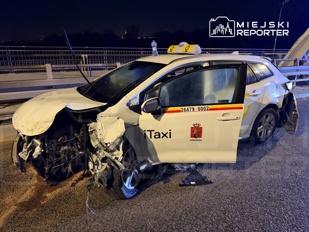 Uszkodzone taksówka stoi na moście, z widocznymi zniszczeniami przodu i otwartymi drzwiami.