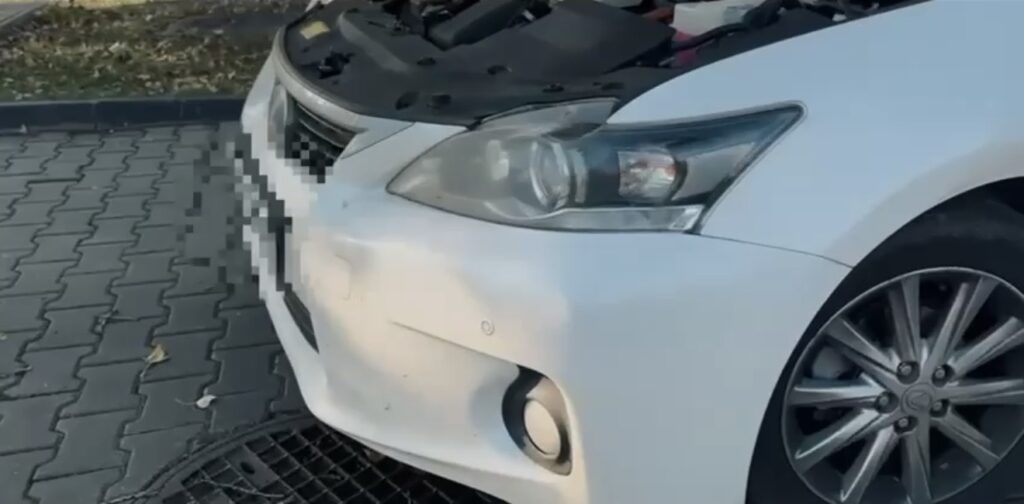 Biały samochód osobowy z otwartą maską stoi na kostkowanej nawierzchni, obok widoczne opadłe liście.