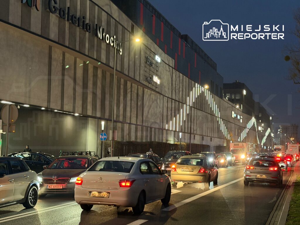 Ruch samochodowy wzdłuż oświetlonego biurowca i centrum handlowego w godzinach wieczornych.
