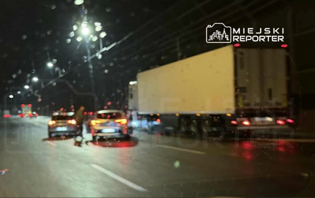 Dwa samochody osobowe zatrzymane na nocnej drodze, z kierowcą rozmawiającym z pasażerem. W tle widoczna ciężarówka.