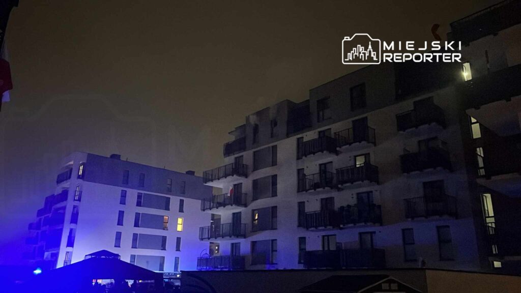 Nowoczesne budynki mieszkalne o jasnych elewacjach w mrocznym otoczeniu, oświetlone niebieskimi światłami.