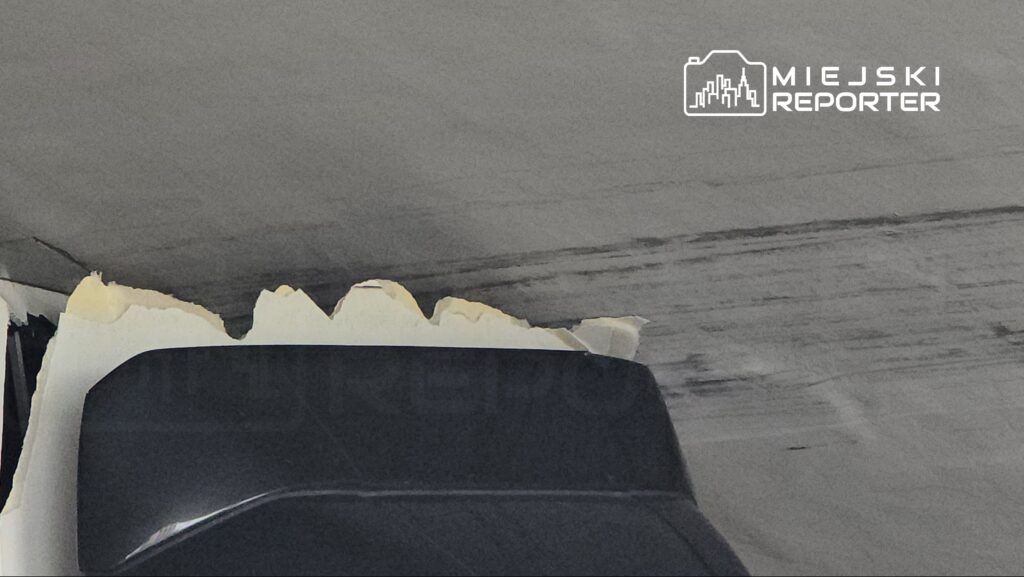 Uszkodzona powierzchnia sufitu z odklejonym fragmentem farby w ciemnym pomieszczeniu.