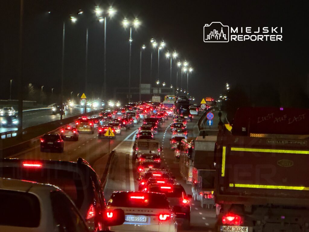 Zator drogowy na oświetlonej autostradzie nocą, z pojazdami stojącymi w korku.