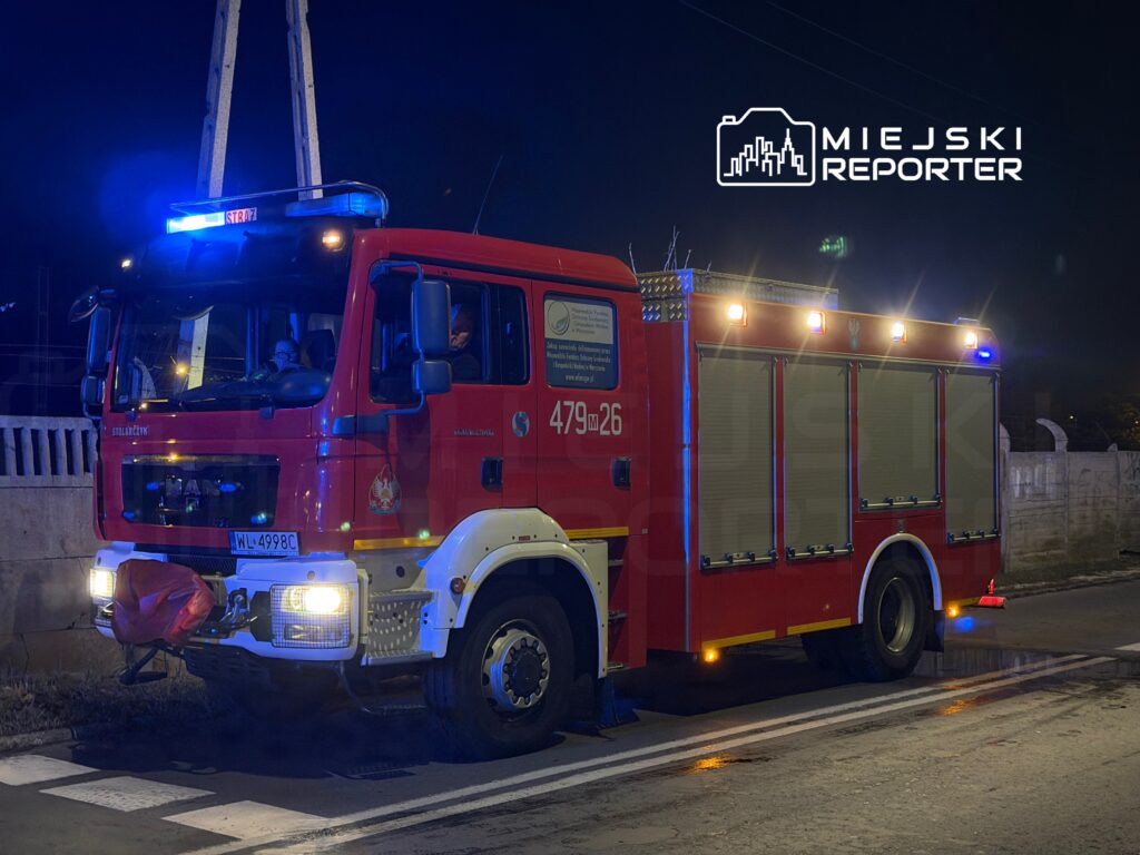 Czerwony wóz strażacki z włączonymi sygnałami świetlnymi stoi na drodze nocą.