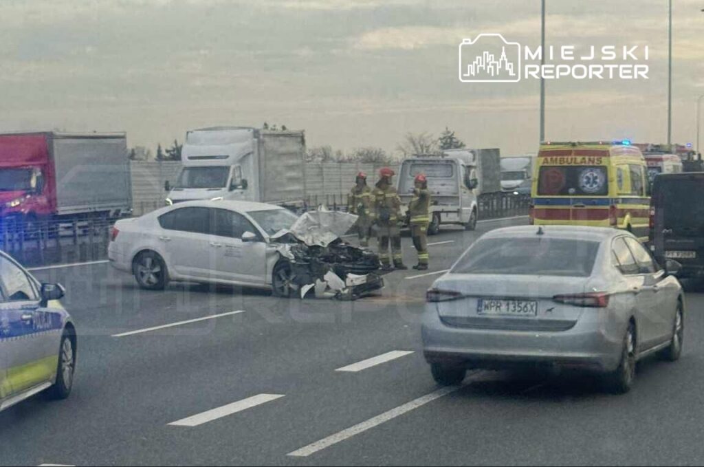 Wielu strażaków ocenia uszkodzenia białego samochodu osobowego na autostradzie po wypadku.