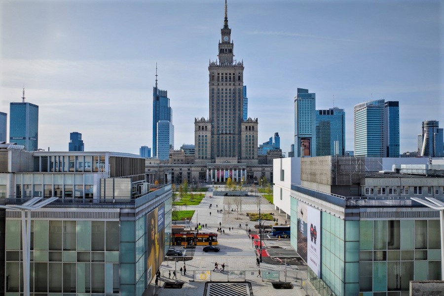Widok na nowoczesne biurowce otaczające Pałac Kultury i Nauki w Warszawie, w tle jasne niebo.