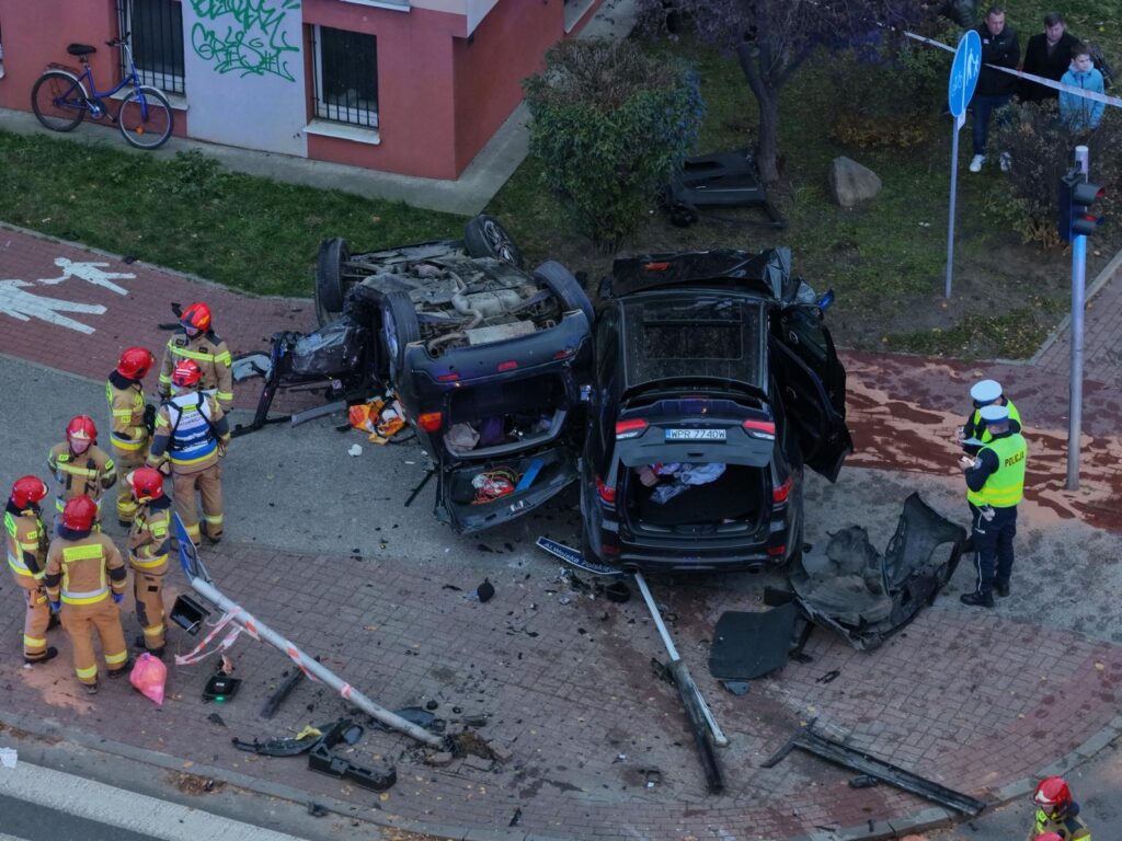 Grupa strażaków w kaskach bada miejsce wypadku drogowego, gdzie dwa pojazdy zderzyły się na skrzyżowaniu.