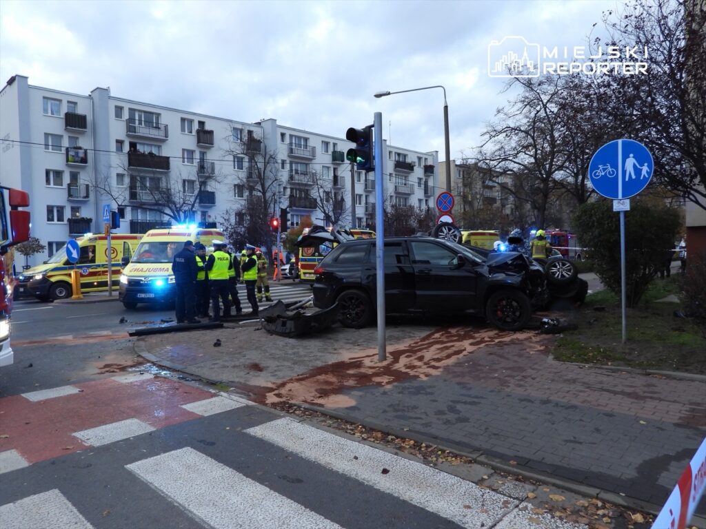 W miejscu wypadku drogowego z udziałem czarnego SUV-a, ratownicy medyczni i policjanci udzielają pomocy.