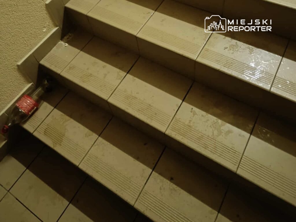 Na schodach widać mokre płytki oraz porzuconą butelkę plastikową.