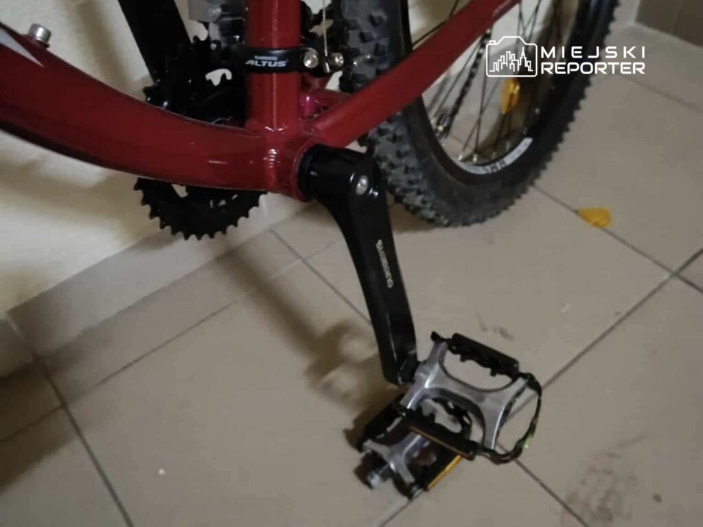 Czerwony rower górski z napędem Shimano i widocznymi pedałami na płaskiej powierzchni podłogi.