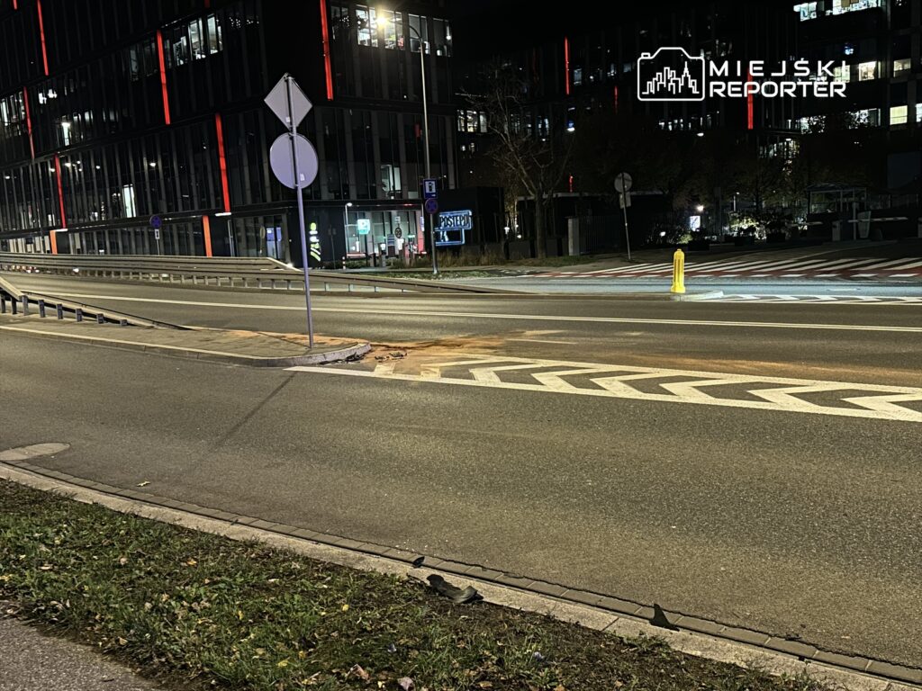 Pusty odcinek drogi z widoczną barierką, znakiem drogowym i żółtym hydrantem w nowoczesnej okolicy nocą.