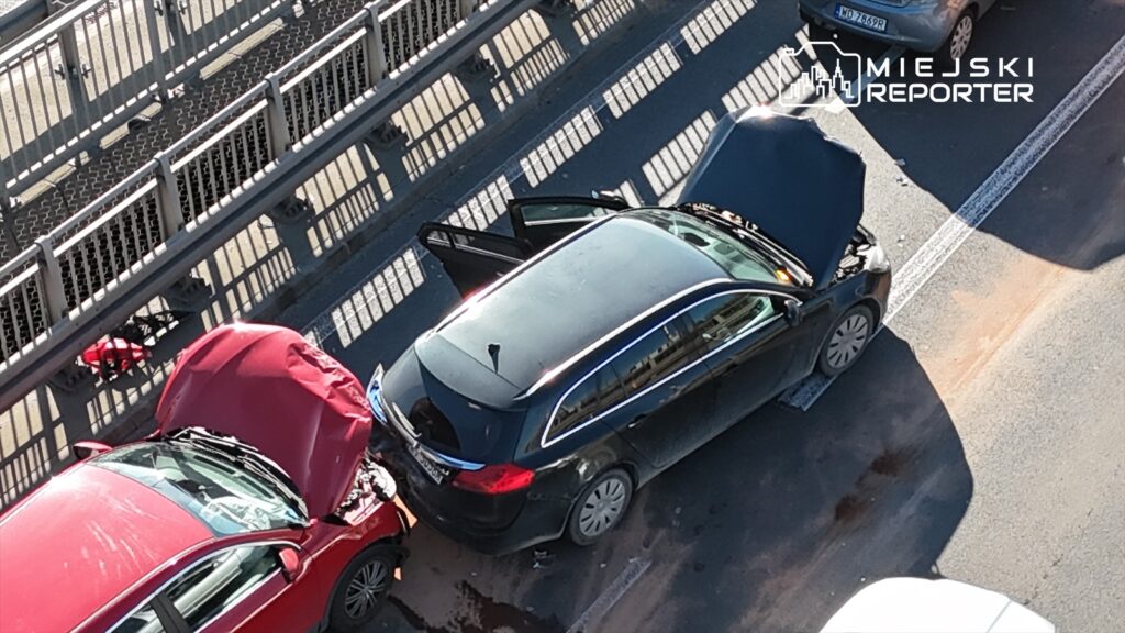 Dwa uszkodzone samochody osobowe na drodze, czerwony z wgnieceniem z przodu i czarny z otwartą maską.