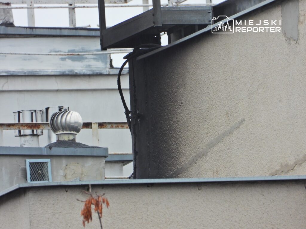 Widok na dach budynku z wentylatorem i śladami uszkodzeń na elewacji.
