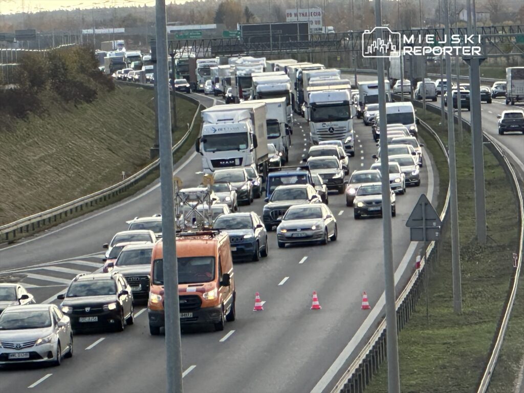 Gęsty ruch samochodowy na drodze ekspresowej, z pojazdem dostawczym i sygnalizacją ostrzegawczą w tle.