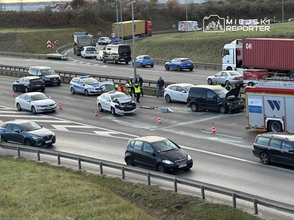 Na autostradzie doszło do wypadku, w którym uczestniczyły dwa uszkodzone samochody, a obok pracują służby ratunkowe.