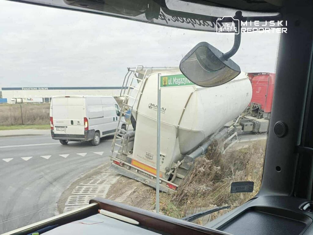Ciężarówka z cysterną utknęła na poboczu drogi, obok białego furgonu w okolicy przemysłowej.