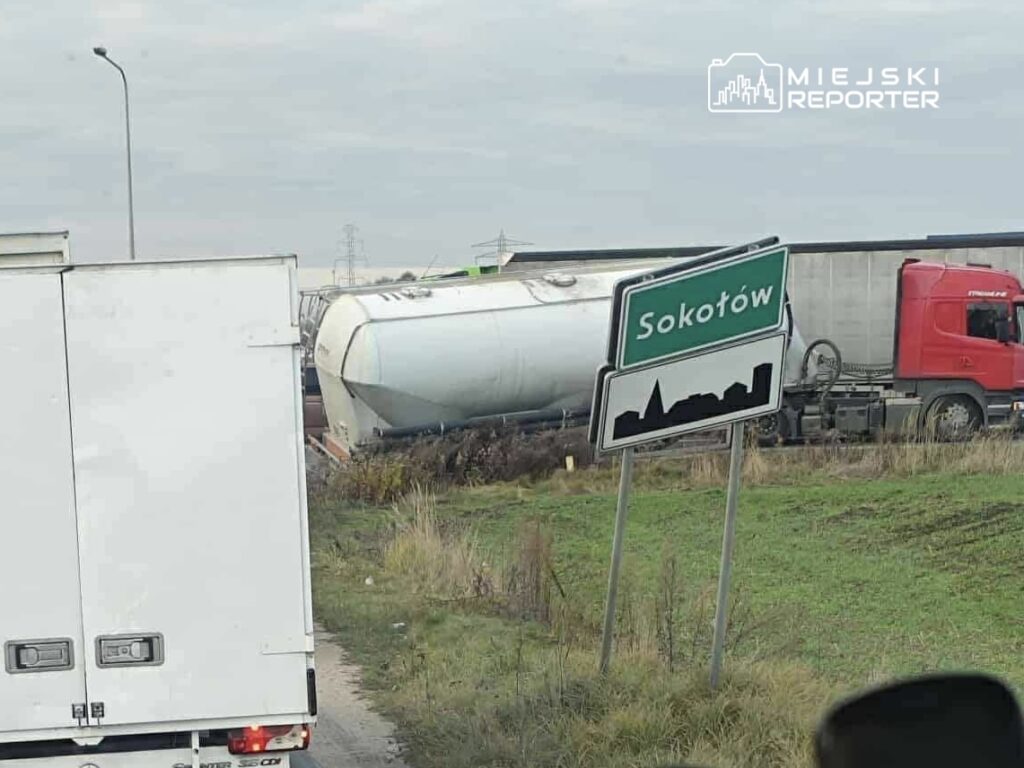 Cysterna przewrócona na poboczu drogi obok znaku miejscowości Sokołów, w tle ciężarówki na drodze.