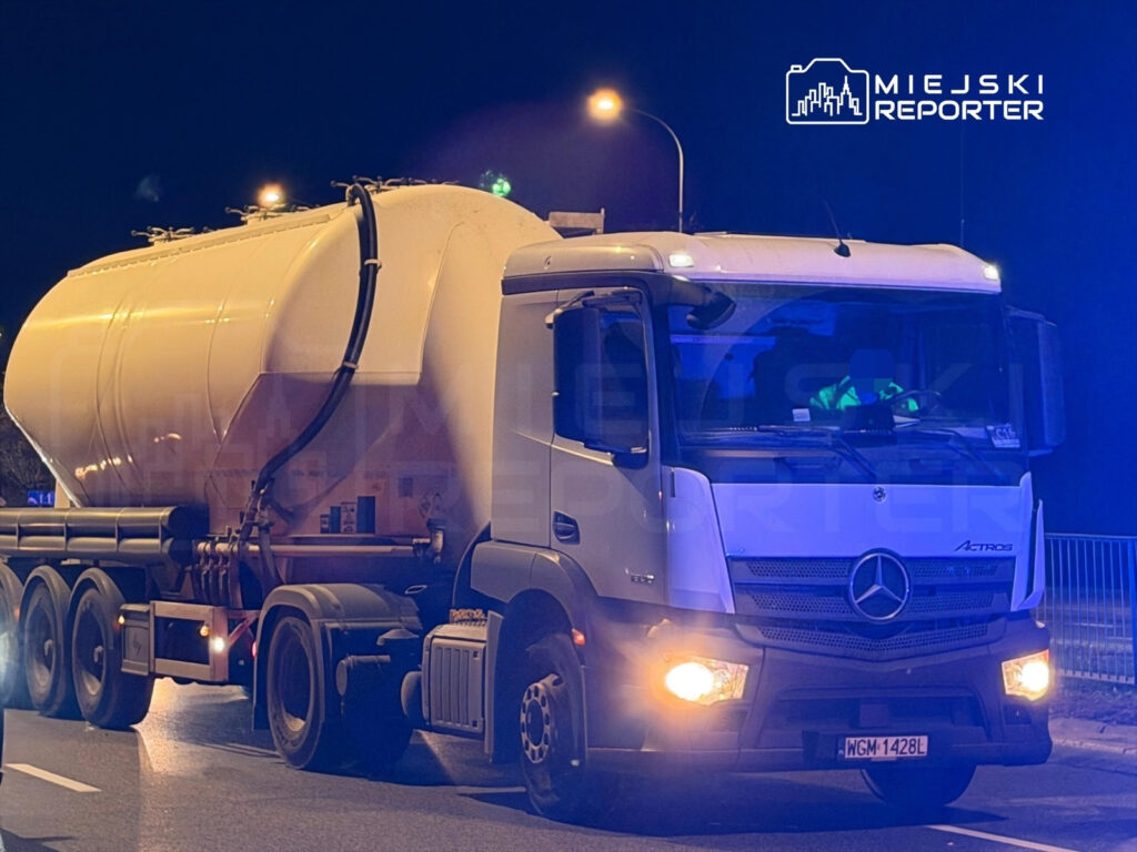 Ciężarówka z dużym zbiornikiem, oświetlona przez latarnie, stoi na drodze w nocy.