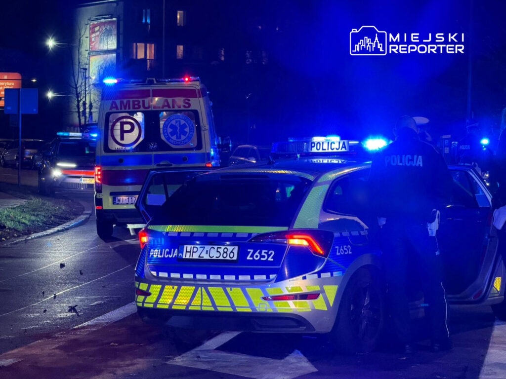 Radiowóz policyjny z włączonymi sygnałami świetlnymi oraz karetka pogotowia na nocnej ulicy.