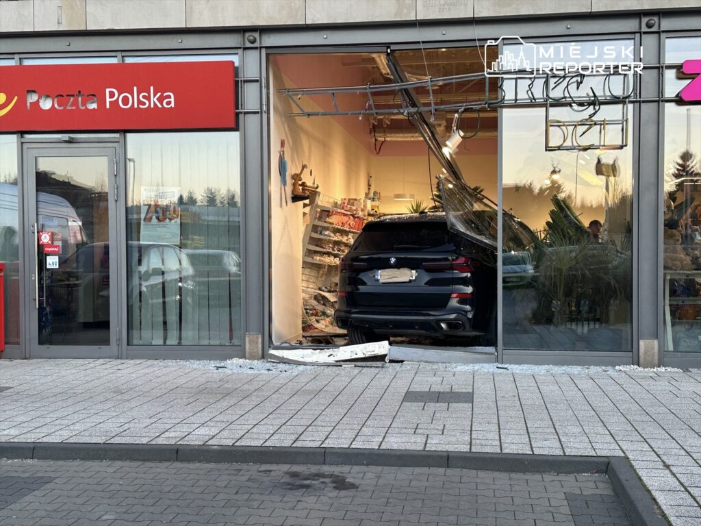 Samochód osobowy wjeżdża do wnętrza sklepu, rozbijając szklane drzwi i zniszczając regały z towarami.