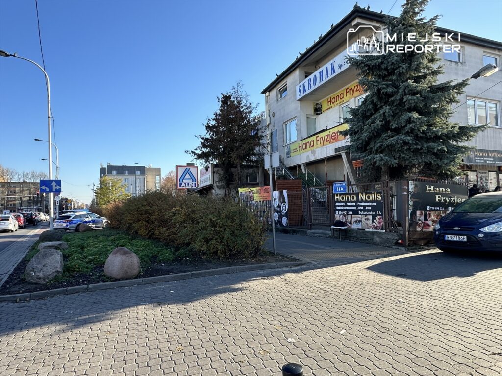 Na rogu ulicy stoi budynek z reklamami salonów fryzjerskich i kosmetycznych, obok znak sklepu ALDI.