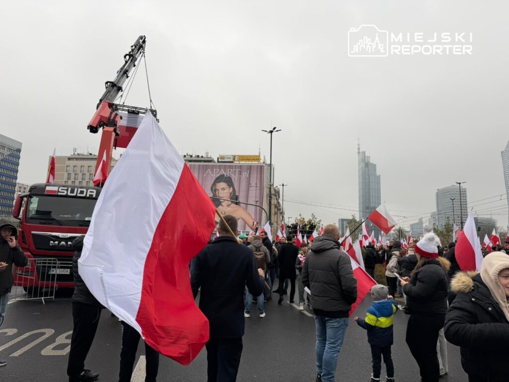 Tłum ludzi z flagami w barwach narodowych uczestniczy w demonstracji na ulicy w miejskim otoczeniu.