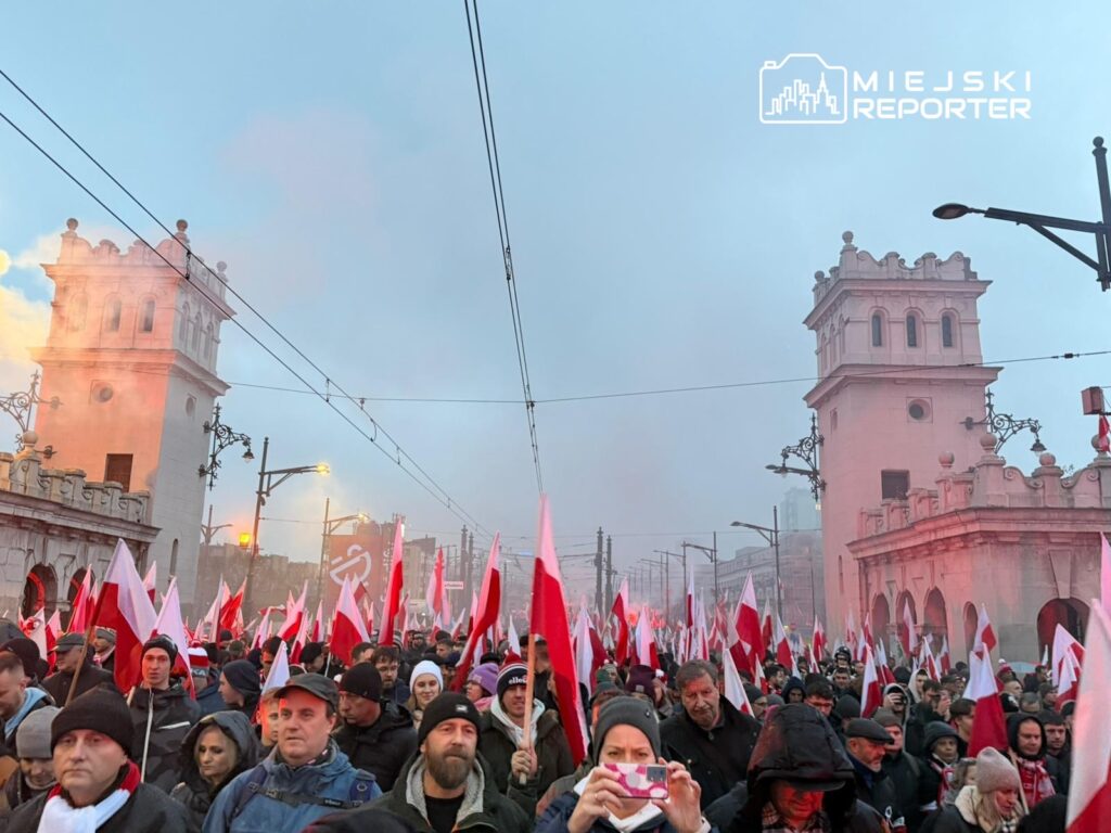 Tłum ludzi z flagami w rękach maszeruje w kierunku zabytkowych budynków w tle, w atmosferze dymu.