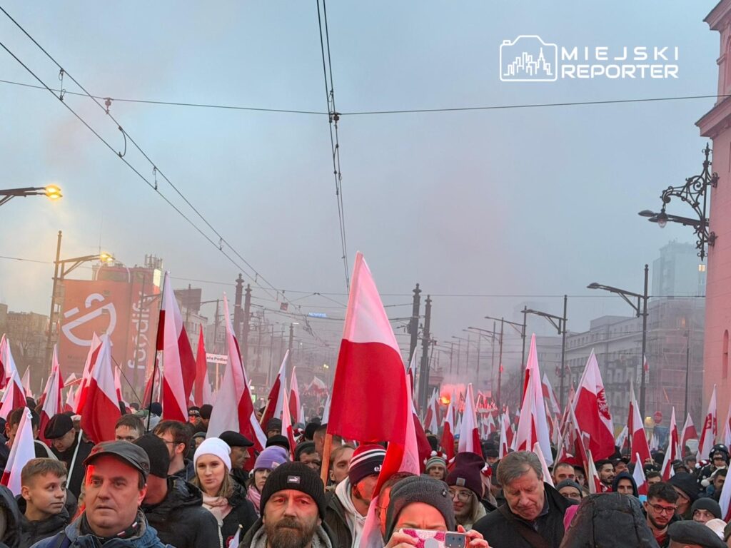 Tłum ludzi z flagami w barwach narodowych, idący ulicą w atmosferze radosnego świętowania.