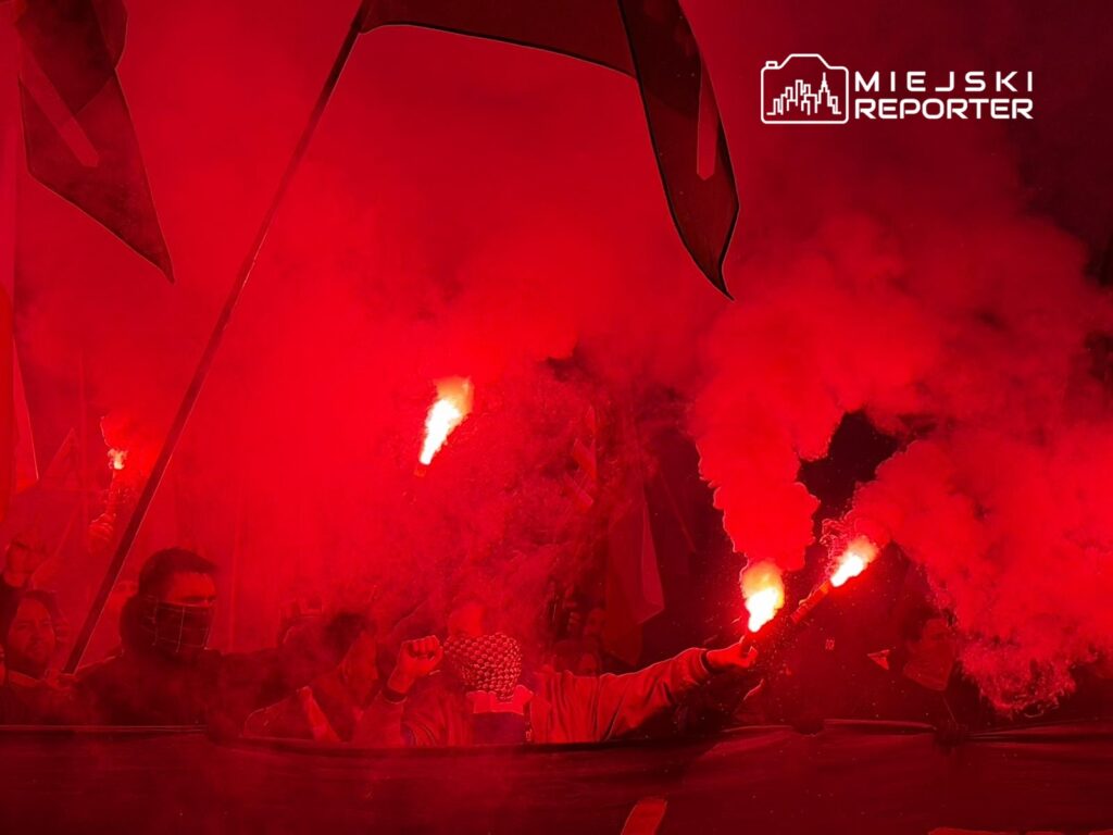 Grupa ludzi z flagami i racami w czerwonym dymie, manifestująca w nocy.