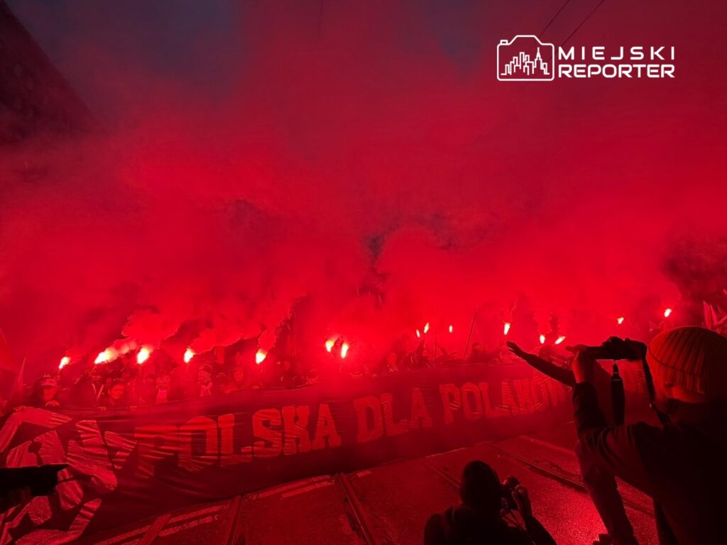 Grupa ludzi z pochodniami i transparentem „POLSKA DLA POLAKÓW” w otoczeniu czerwonego dymu na ulicy.