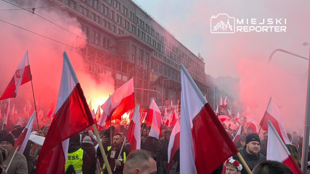 Tłum ludzi trzymających flagi w barwach narodowych, otoczony dymem z rac, na ulicy w mieście.