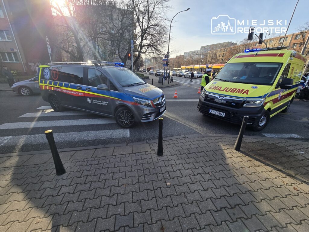 Zespół transplantacyjny oraz karetka pogotowia zatrzymane na przejściu dla pieszych w miejskim otoczeniu.