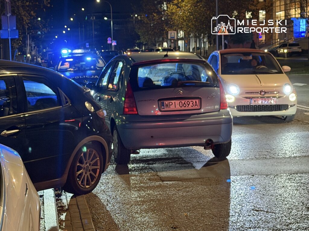 Policyjny radiowóz z włączonymi sygnałami świetlnymi stojący obok zderzonych samochodów na ulicy nocą.